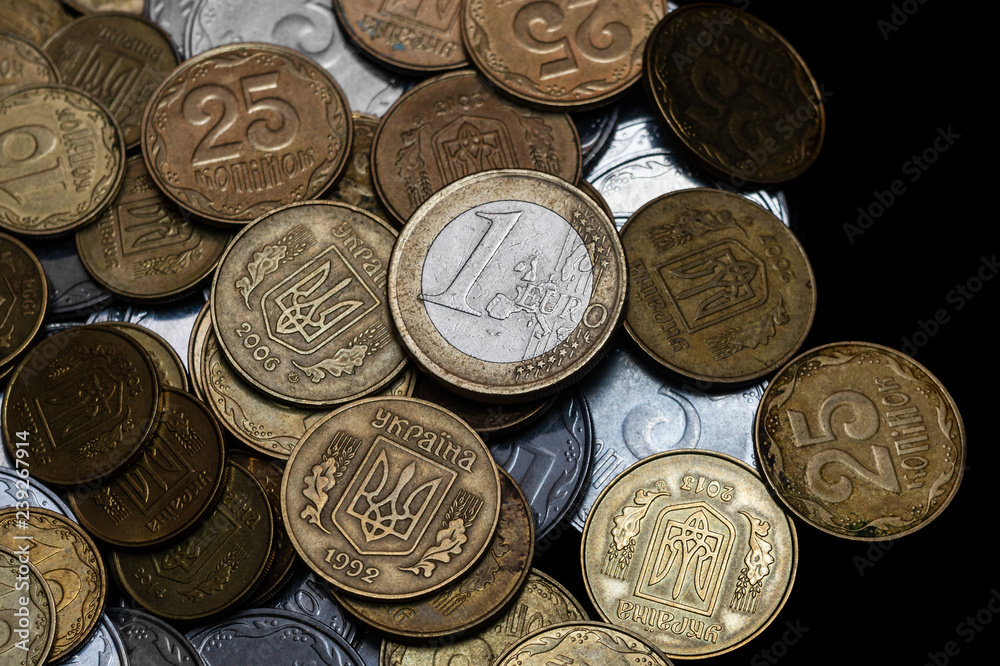 Ukrainian coins with one euro coin isolated on black background. Close-up view. Coins are located at center of frame. A conceptual image. Ukrainian coins with one euro coin isolated on black background. Close-up view. Coins are located at center of frame. A conceptual image.