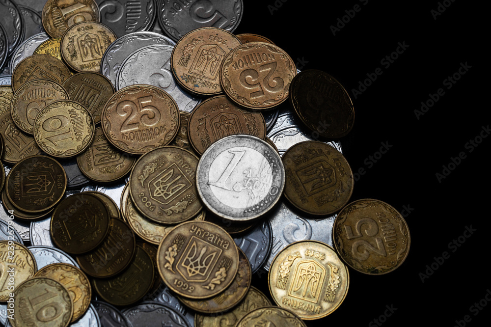 Ukrainian coins with one euro coin isolated on black background. Euro coin is uncolored. Close-up view. Coins are located at the left side of frame. A conceptual image. Ukrainian coins with one euro coin isolated on black background. Euro coin is uncolored. Close-up view. Coins are located at the left side of frame. A conceptual image.