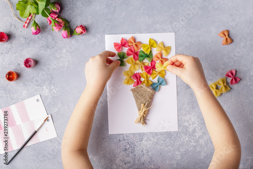 Paper crafts for mother day, 8 march or birthday. Small child doing a bouquet of flowers out of colored paper and colored pasta for mom. Simple gift idea. view top, copy space