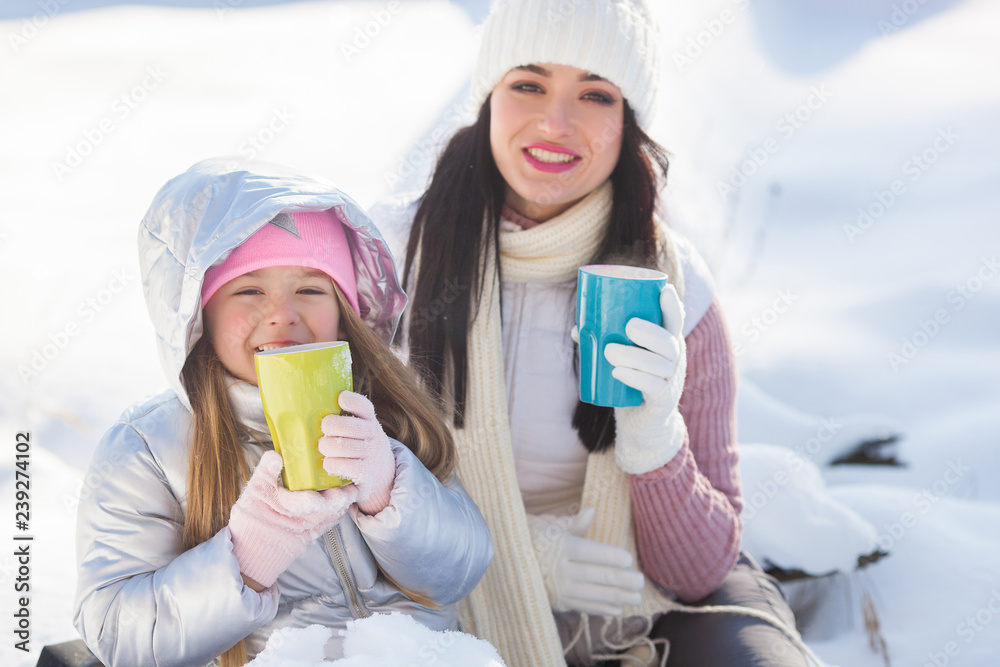Mother and her daughter having fun outdoors in winter time. Pretty family drinking tea and cocoa Mother and her daughter having fun outdoors in winter time. Pretty family drinking tea and cocoa