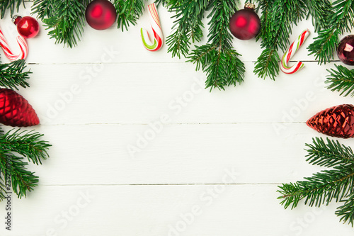 Fresh fluffy fir tree branches red ornament balls candy canes on white plank wood backdrop. Styled Christmas New Year background greeting card poster banner template