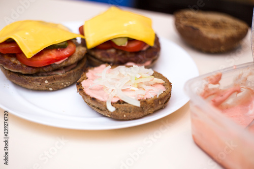 Preparing delicious burgers. Chef cooking meat burgers with bacon, cheese and vegetables, selective focus. Close-up.