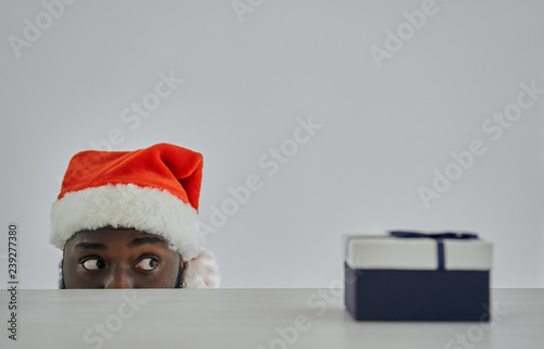 Tapet The african man in the santa hat watching from the table with a gift