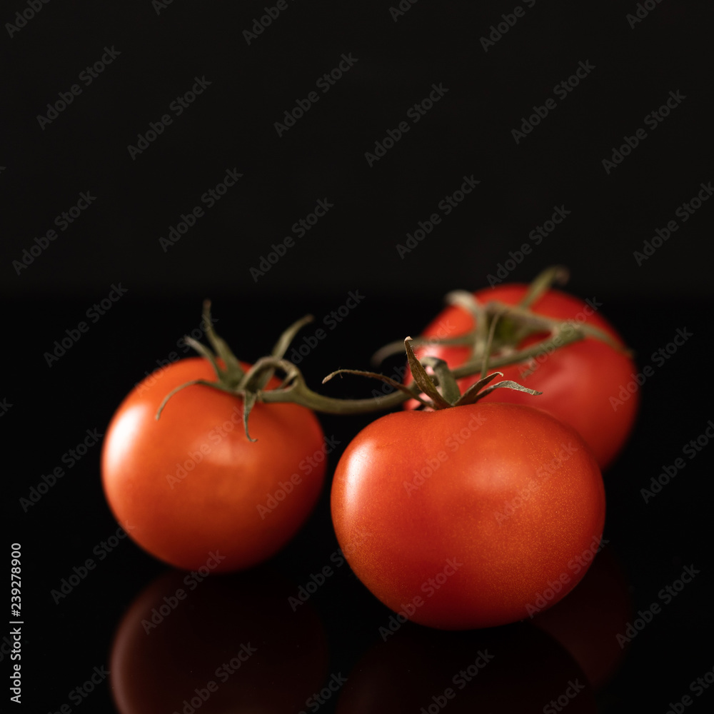 Tomatoes on a branch. Tomatoes on the vine and on a black glass background with reflection