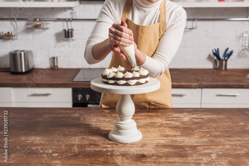 Φωτογραφία cropped shot of woman in apron decorating delicious sweet cake with cream