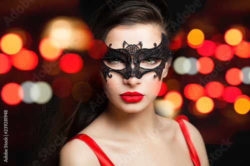 Gorgeous woman in black carnival mask on colorful night glitter bokeh background