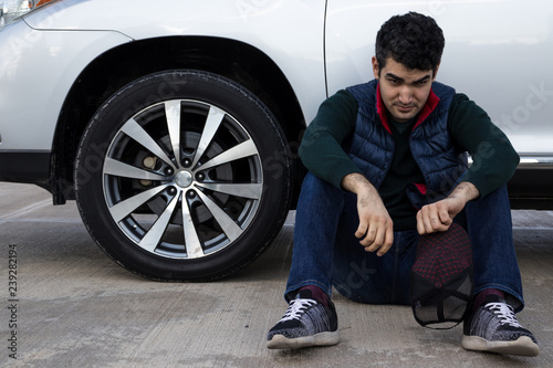 depressed man sitting on a ground leaning on his broken car. Sad, angry and frustrated person. Emergency.
