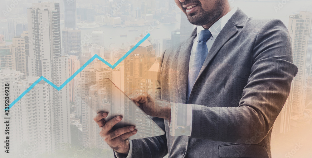 businessman in suit holding tablet standing over blurred city background and successful graph foreground. Double exposure businessman in suit holding tablet standing over blurred city background and successful graph foreground. Double exposure