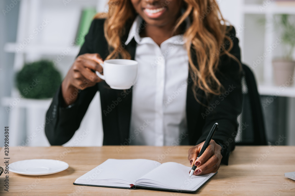 cropped view of african american businesswoman writing in notebook in office cropped view of african american businesswoman writing in notebook in office