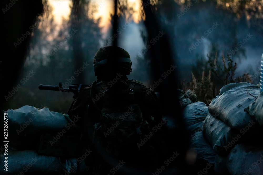 Sniper armed with large caliber, sniper rifle, shooting enemy targets on range from shelter, sitting in ambush. Back view Sniper armed with large caliber, sniper rifle, shooting enemy targets on range from shelter, sitting in ambush. Back view