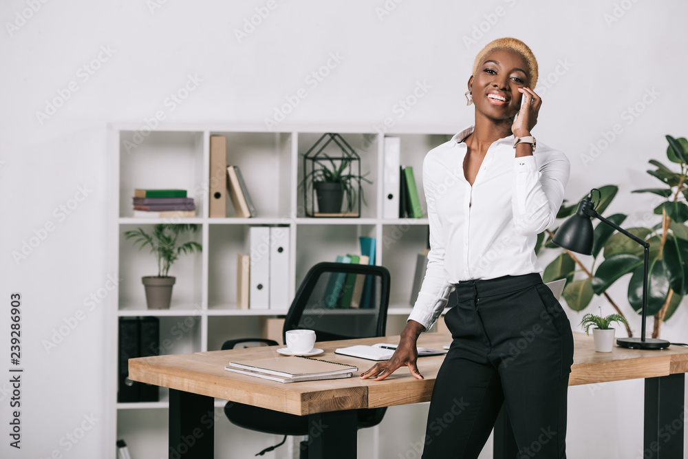 happy african american businesswoman with short hair talking on smartphone in modern office happy african american businesswoman with short hair talking on smartphone in modern office