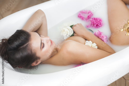 Young beautiful woman taking bath with flowers and milk. Attractive girl making spa procedure. Body care. Female taking aroma bath with peony
