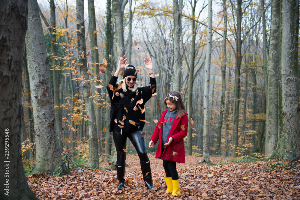 Cute girl and mom playing with leaves in the forest at autumn Cute girl and mom playing with leaves in the forest at autumn
