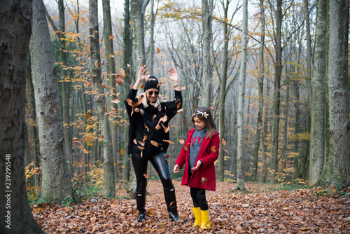 Cute girl and mom playing with leaves in the forest at autumn