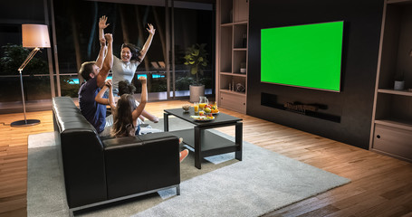 A family is watching a TV and celebrating some joyful moment, sitting on the couch in the living room.