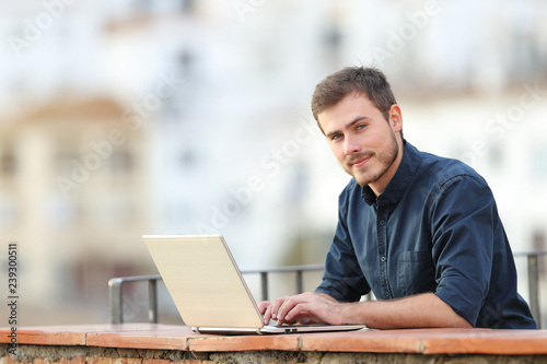 Man using a laptop and looking at camera in a balcony photo