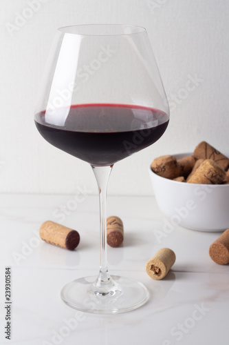 a glass of red wine and wine corks on a white background.