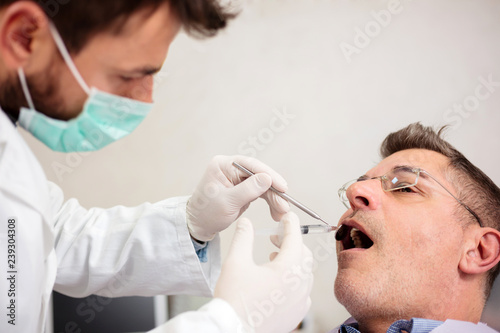 Young male dentist holding a syringe  giving anesthetic to a mature male patient. Health care and medicine concept.