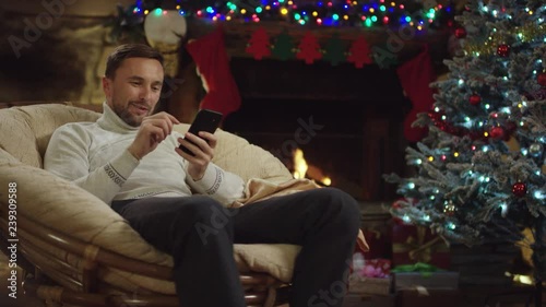 Respectuf adult man texing in messenger on smartphone in Christmas night by decorated tree photo