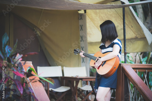 Happy young cute asian girl hipster playing guitar at tent camping campfire party while travelling at beautiful sky mountains scenery views 