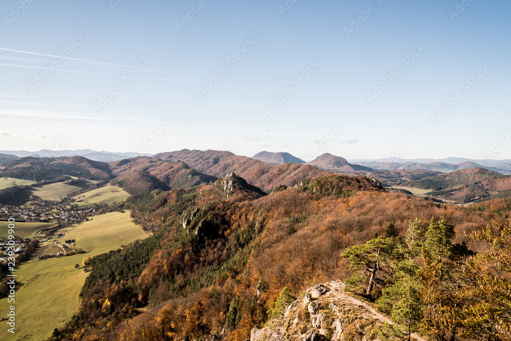 view from Stefanikova vyhliadka view point in autumn Sulovske skaly mountains with hills covered by colorful forest and valley with village and meadows
