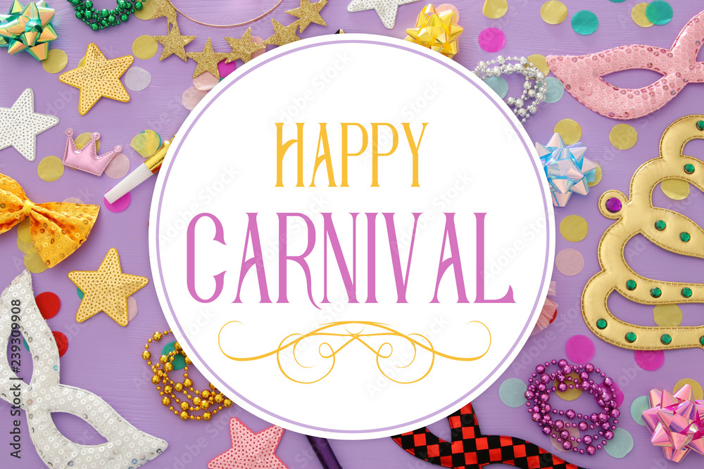 carnival party celebration concept with masks and colorful party accessories over pink, purple wooden background. Top view.