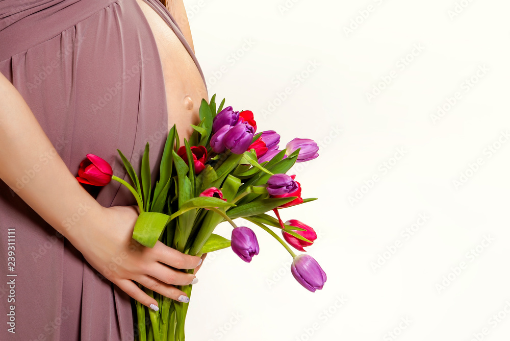 pregnancy. Exposed belly and hands of a pregnant woman. Spring flowers. Tulips.