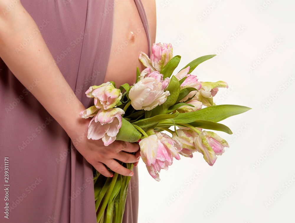 pregnancy. Exposed belly and hands of a pregnant woman. Spring flowers. Tulips.