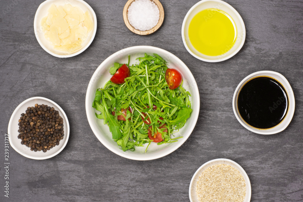 Mixed arugula leaves and sliced cherry tomatoes. recipe step by step arugula salad in a grey ceramic bowl flatlay on grey stone Mixed arugula leaves and sliced cherry tomatoes. recipe step by step arugula salad in a grey ceramic bowl flatlay on grey stone