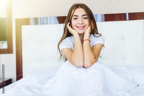 Smiling young woman sitting in bed in the morning at home and looking away