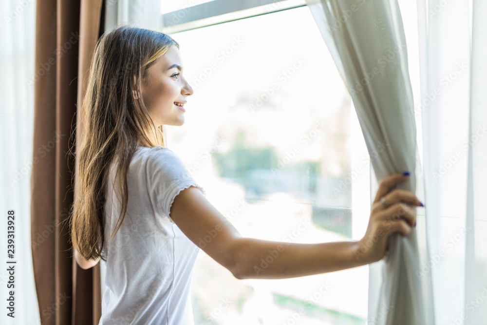 Young pretty girl opening curtains in a bedroom