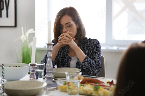 Young woman praying before meal at home