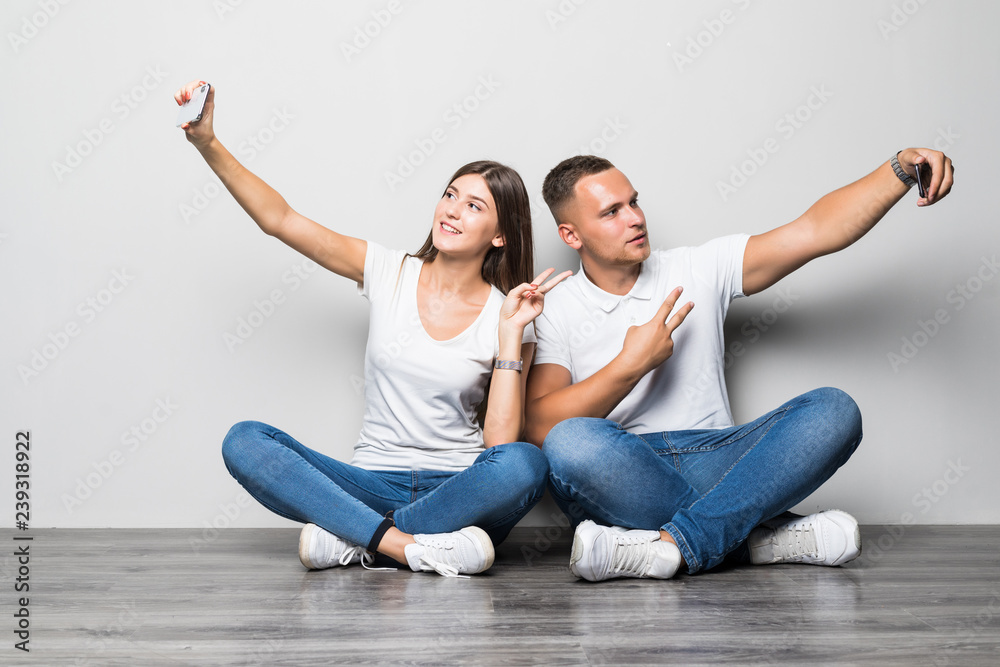 Portrait of a happy young couple taking selfies sitting together over beige background Portrait of a happy young couple taking selfies sitting together over beige background