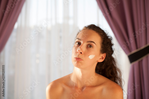 Close up beauty portrait of a laughing beautiful half naked woman applying face cream and looking away