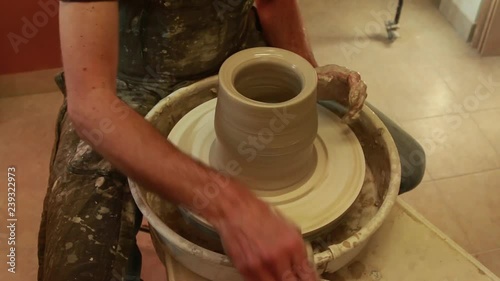 Artist potter in the workshop creating a jug out of earthenware, hands closeup. Twisted potter's wheel. Small aristic craftsmen business concept.  photo