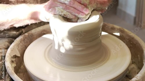 Artist potter in the workshop creating a jug out of earthenware, hands closeup. Twisted potter's wheel. Small aristic craftsmen business concept.  photo