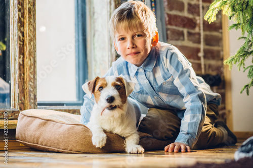 Cute little kid boy with best friend Jack russel terrer dog huugging and looking at camera near the window together. School age boy and dog at home, winter day, cozy lifestyle concept. photo