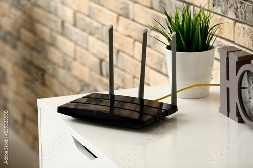 Modern wi-fi router on light commode near brick wall photo