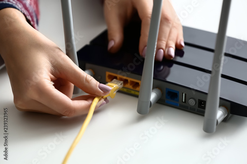Woman inserting ethernet wire into wi-fi router on white table, closeup photo