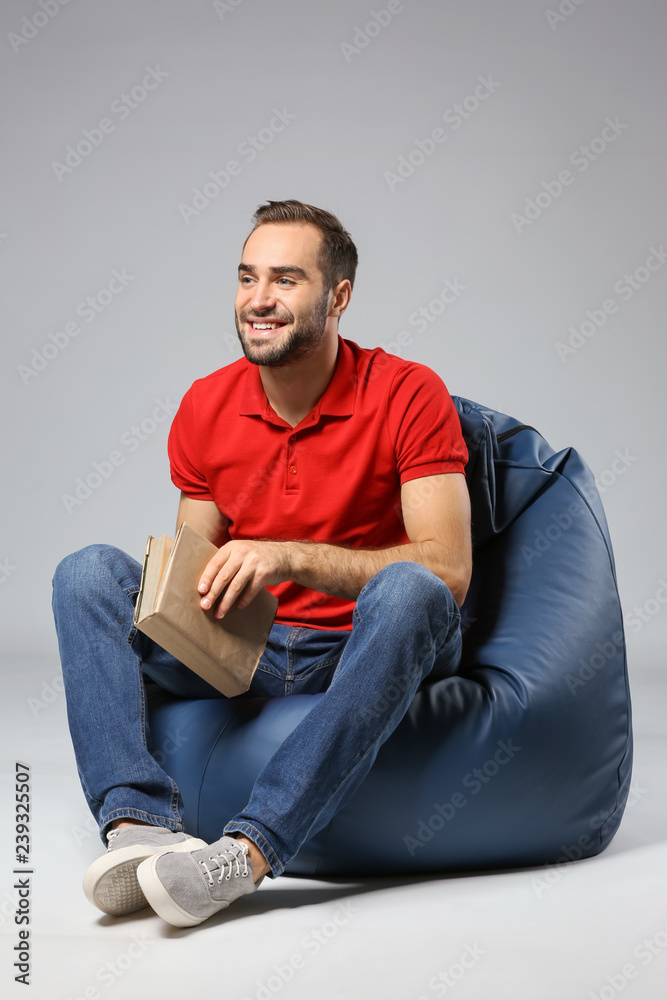 Young man with book sitting on beanbag chair against grey background Young man with book sitting on beanbag chair against grey background
