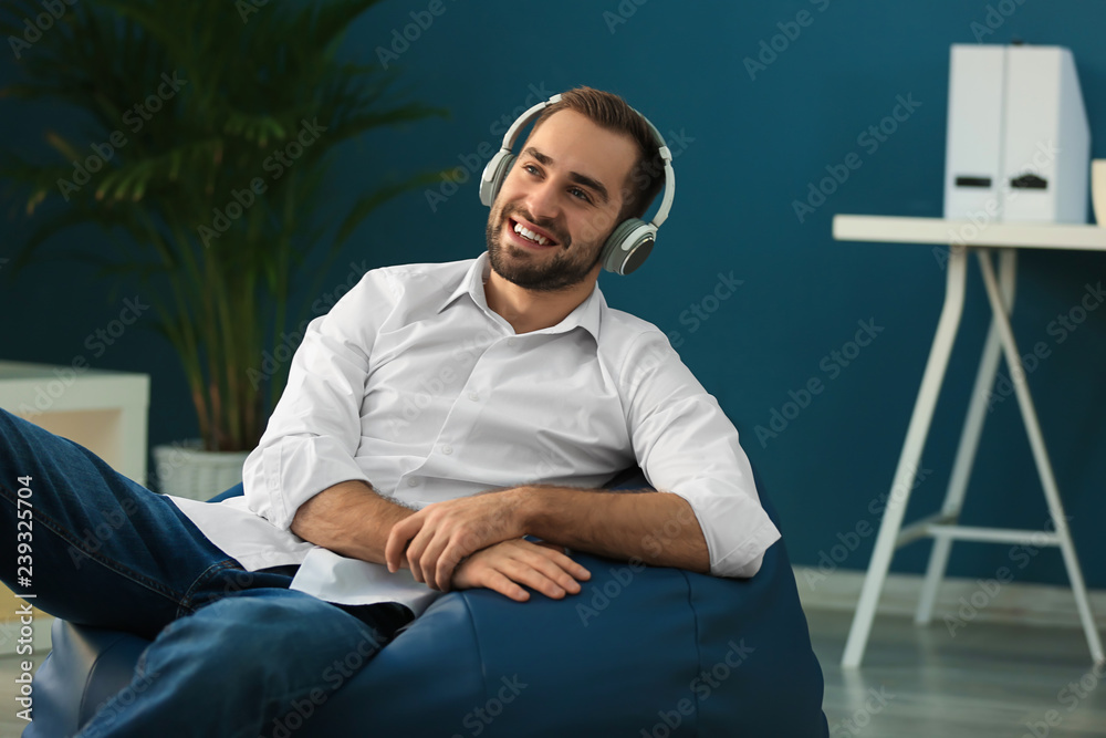 Fototapeta premium Young businessman with headphones sitting on beanbag chair in office