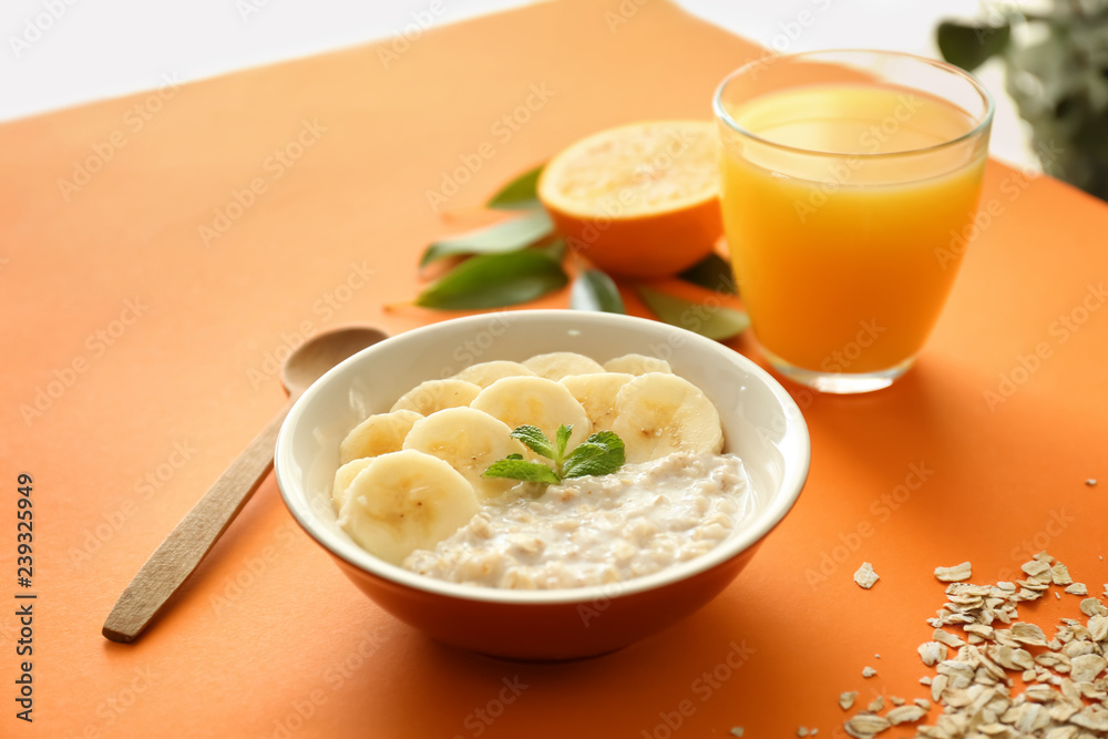 Tasty oatmeal with banana slices in bowl and glass of orange juice on color table Tasty oatmeal with banana slices in bowl and glass of orange juice on color table