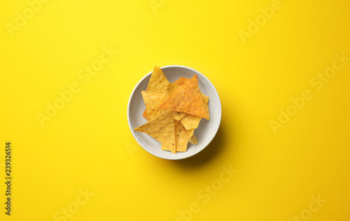 Bowl with tasty corn chips on color background