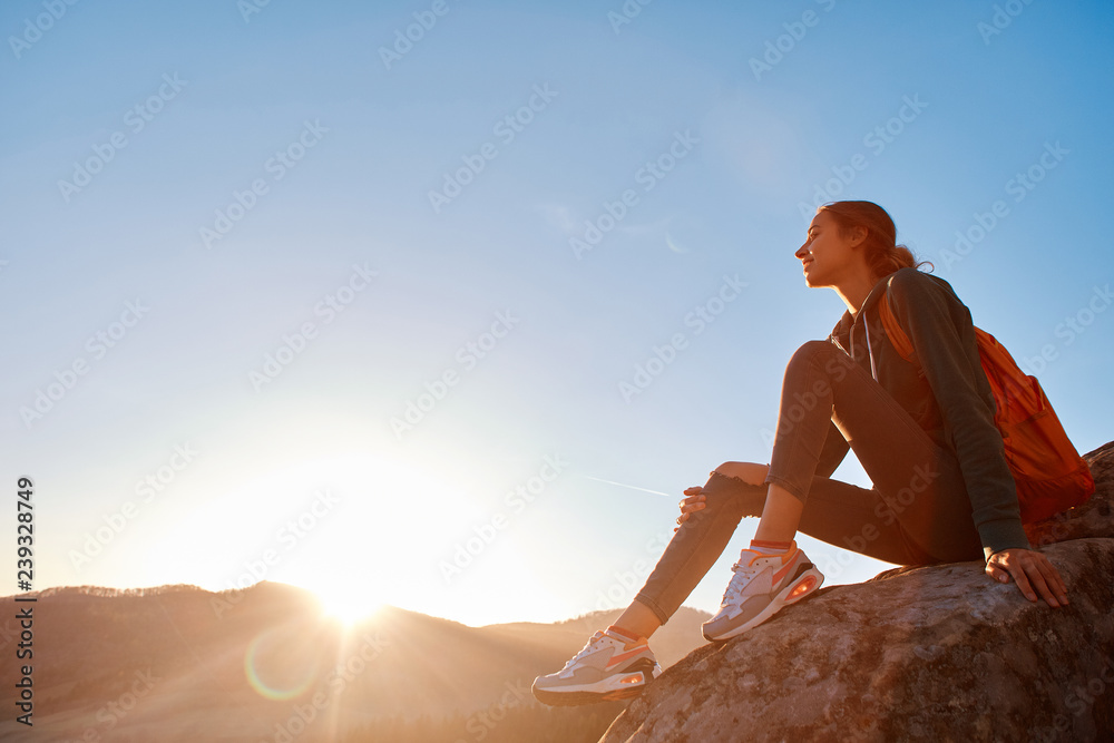 woman sits on edge of cliff against background of sunrise woman sits on edge of cliff against background of sunrise