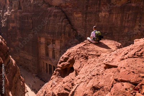 Aerial view of Treasury with a tourist, hiker, solo traveler, young man backpacker seated on a cliff, Al Khazneh in the ancient city of Petra, Jordan, UNESCO World Heritage Site