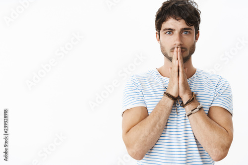 Waist-up shot of hopeful and sincere good-looking caucasian masculine guy acting intense, nervous standing seriously over gray background with hands in pray over lips, acting worried and sympathizing