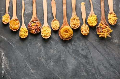 Spoons with different types of raw pasta on grey table