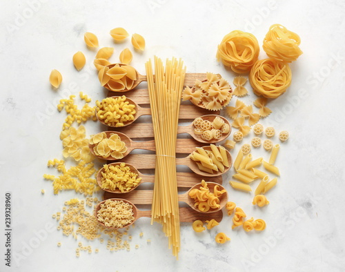 Spoons with different types of raw pasta on white table