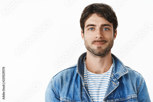Handsome guy feeling confident and upbeat getting ready for interview smiling sincere and self-assured with joyful mood standing in trendy denim jacket against gray wall with enthusiastic expression photo