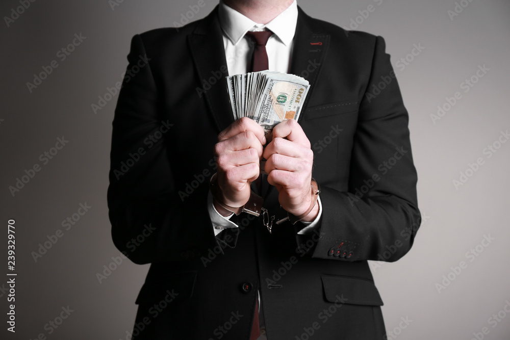 Businessman in handcuffs with bribe on grey background. Corruption concept Businessman in handcuffs with bribe on grey background. Corruption concept